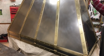 A burnished stainless & brass hood for a modern or traditional classic kitchen nearing completion in the shop. The burnished stainless has a more satin look than polished metal.